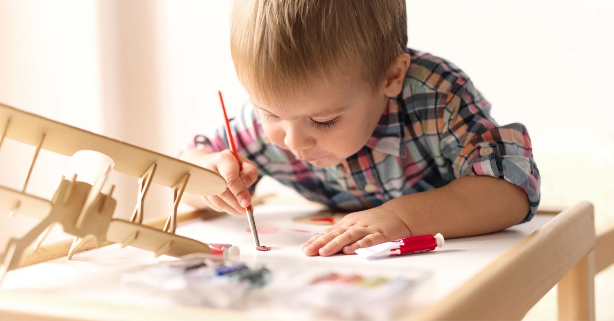 boy painting a wooden airplane